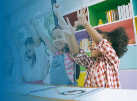 Early childhood students working at a table and raising their hands excited.